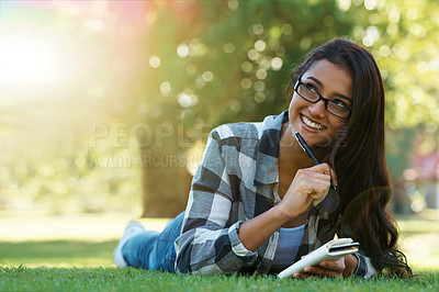 Buy stock photo A young woman lying on the grass writing in a notebook