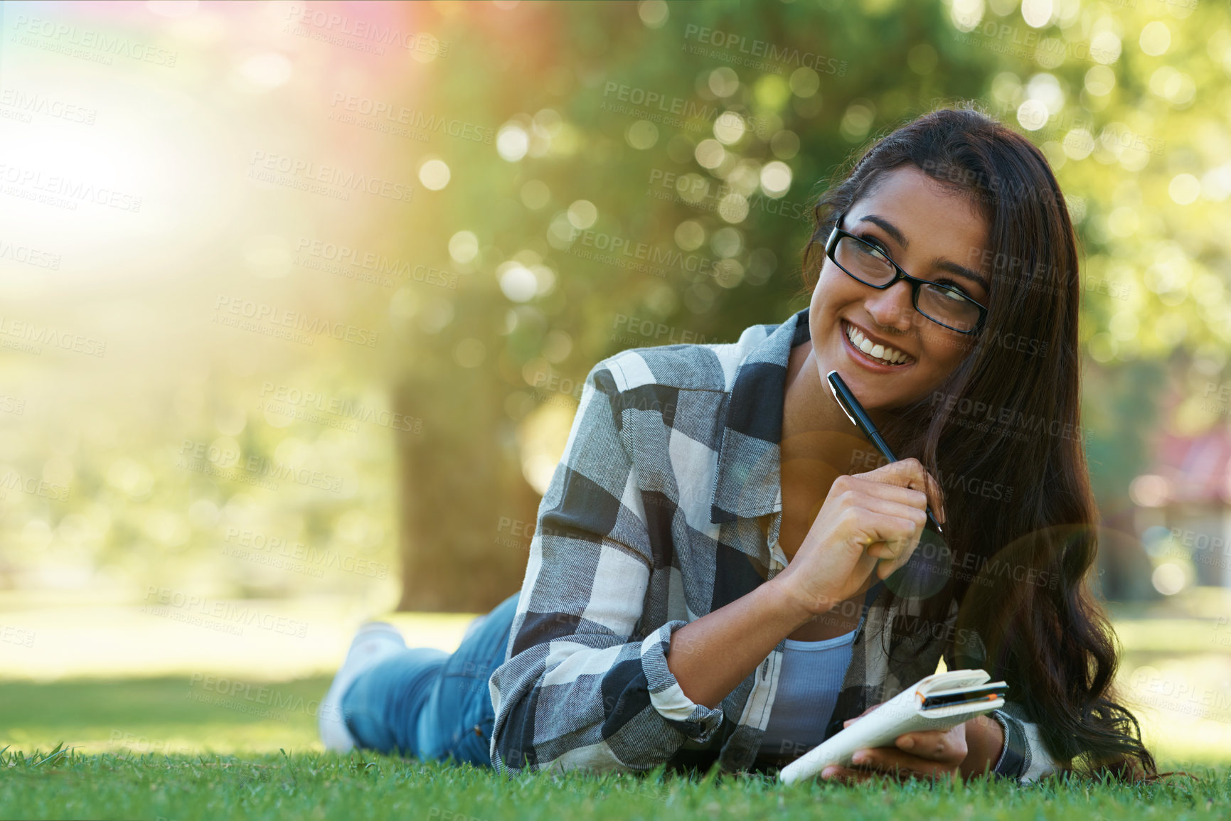 Buy stock photo A young woman lying on the grass writing in a notebook