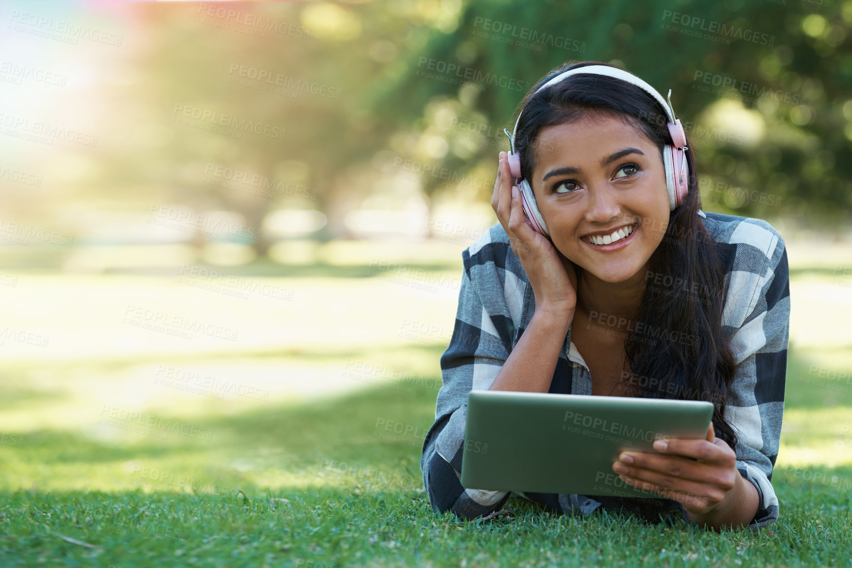 Buy stock photo Woman, headphones and streaming podcast on tablet, learning and internet for education on grass in outdoors. Female person, happy and relaxing on lawn, knowledge and student subscription for info