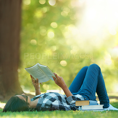 Buy stock photo Shot of a young woman lying on grass and reading a book
