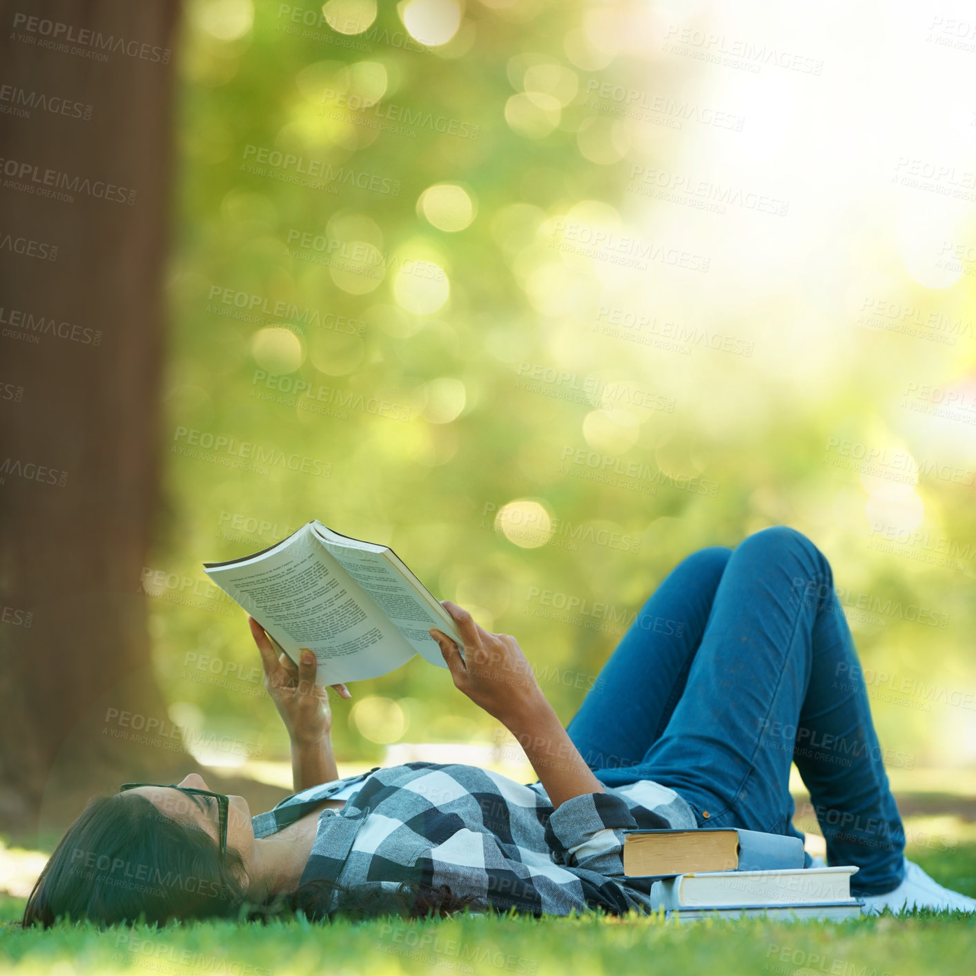 Buy stock photo Shot of a young woman lying on grass and reading a book