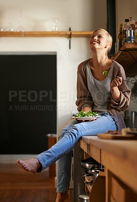 Buy stock photo Shot of an attractive young woman sitting on her kitchen counter laughing while eating a salad