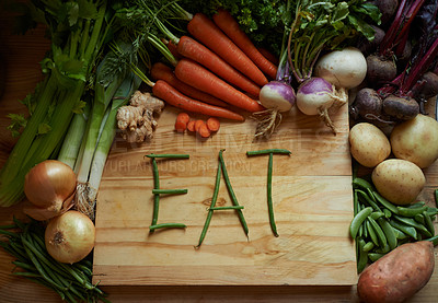 Buy stock photo Vegetables, chopping board and kitchen with variety ingredients with the message 'eat'. High angle, fresh from the earth and healthy green foods, herbs or organic produce harvest on wooden piece 