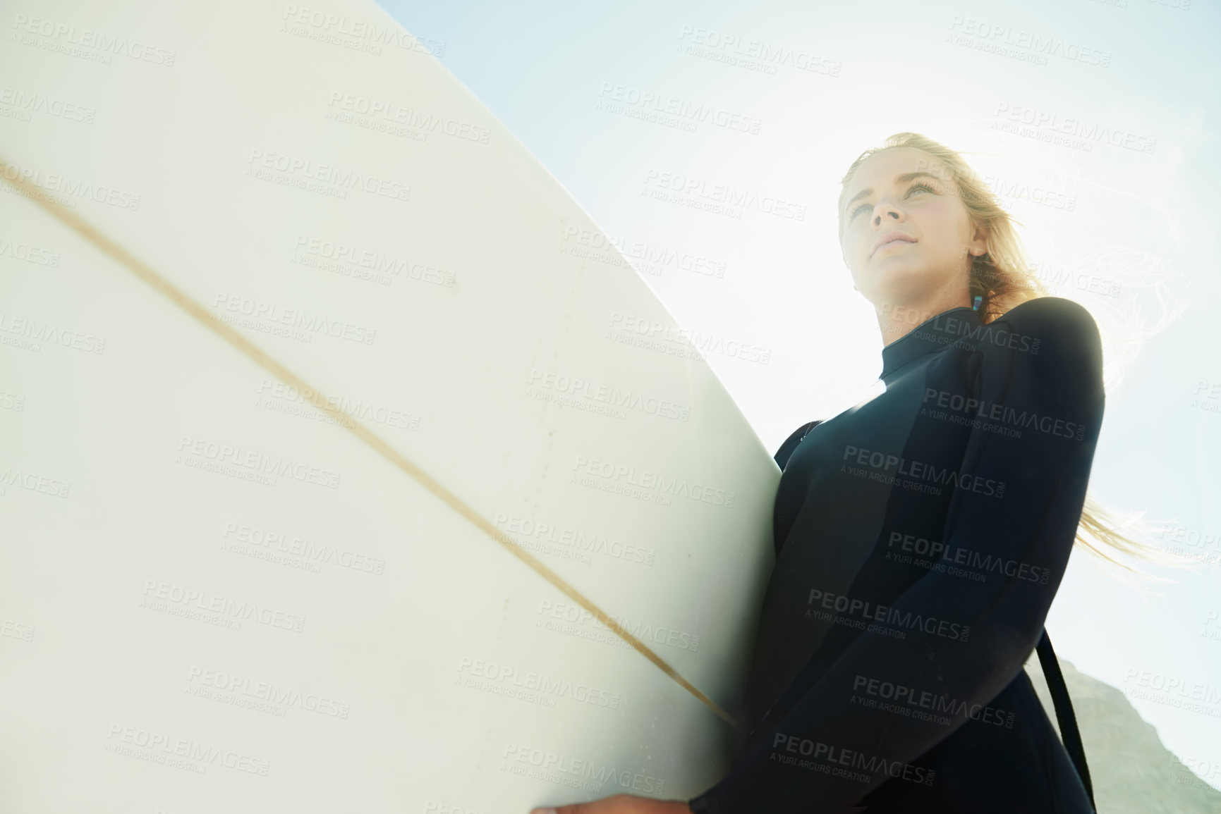 Buy stock photo Face, flare and woman on beach with surfboard from below for travel, vacation or adventure on coast in summer. Nature, fitness or exercise with confident young surfer person in wetsuit for recreation