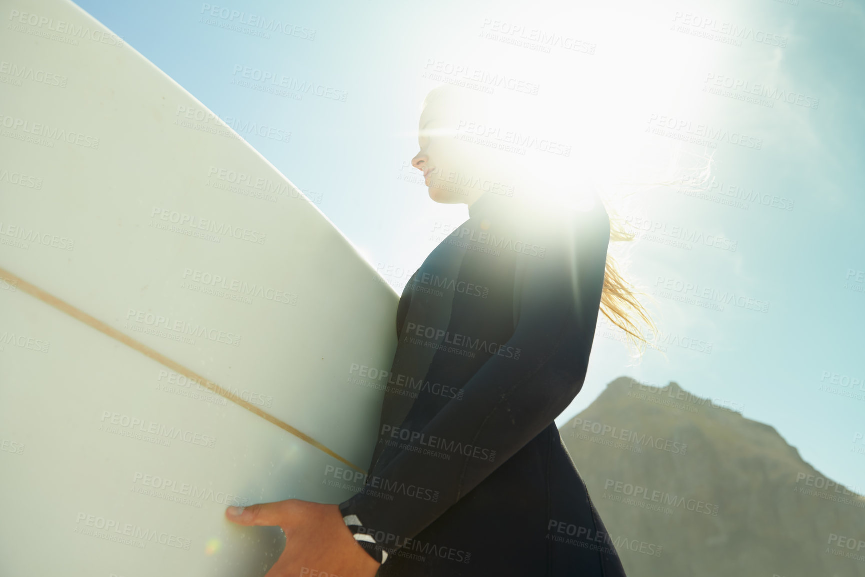 Buy stock photo Flare, sky at beach and woman with surfboard in summer from below for travel, vacation or holiday. Exercise, fitness or sports with confident young surfer person in wetsuit for leisure closeup