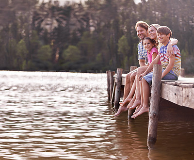 Buy stock photo A happy family of four sitting on a jetty at the lake