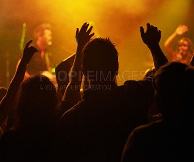 Buy stock photo Fans, hands and silhouette, people at concert or music festival from back, orange lights and energy at live event. Dance, fun and excited crowd in arena at rock band performance or audience dancing.