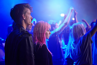 Buy stock photo Couple in crowd, man and woman at music festival, neon lights and watching live band performance on stage. Dance, group of people at party and blue lighting, fans on date at rock concert together.