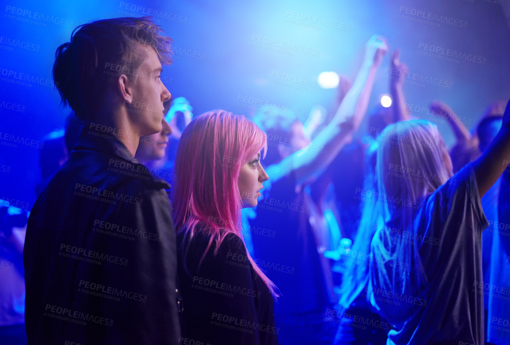 Buy stock photo Couple in crowd, man and woman at music festival, neon lights and watching live band performance on stage. Dance, group of people at party and blue lighting, fans on date at rock concert together.