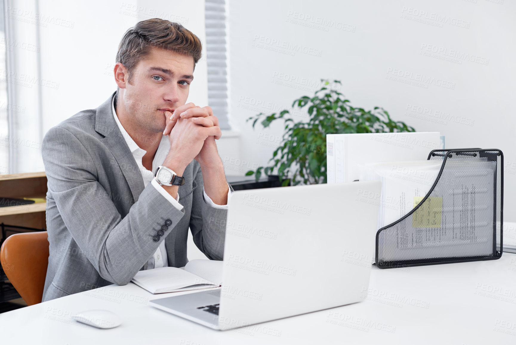 Buy stock photo A serious young businessman sitting at his desk and considering his options