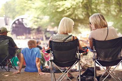 Buy stock photo Back, friends sitting and outdoor festival on camping chair, talking and women in audience, concert or music performance. People, fans relaxing together or summer show, entertainment or culture event