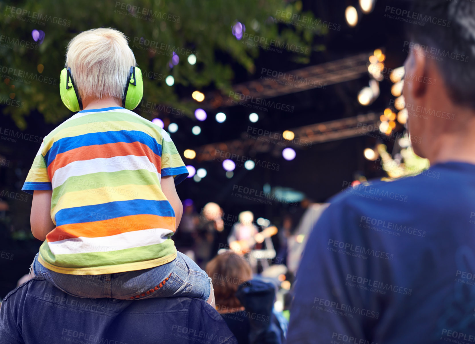 Buy stock photo Rearview shot of a young boy sitting on his father's shoulders at a music concert