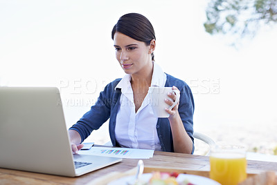 Buy stock photo An attractive young woman working on her laptop with her breakfast in focus