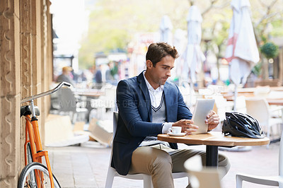 Buy stock photo Shot of a young businessman sitting at an outdoor cafe using a digital tablet