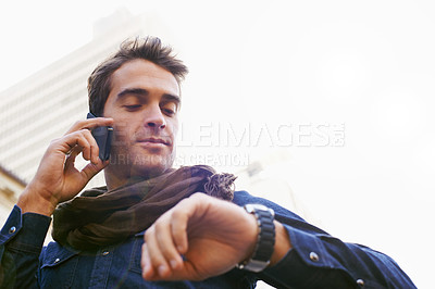 Buy stock photo Low angle shot of a man chekcing his watch while talking on his cellphone