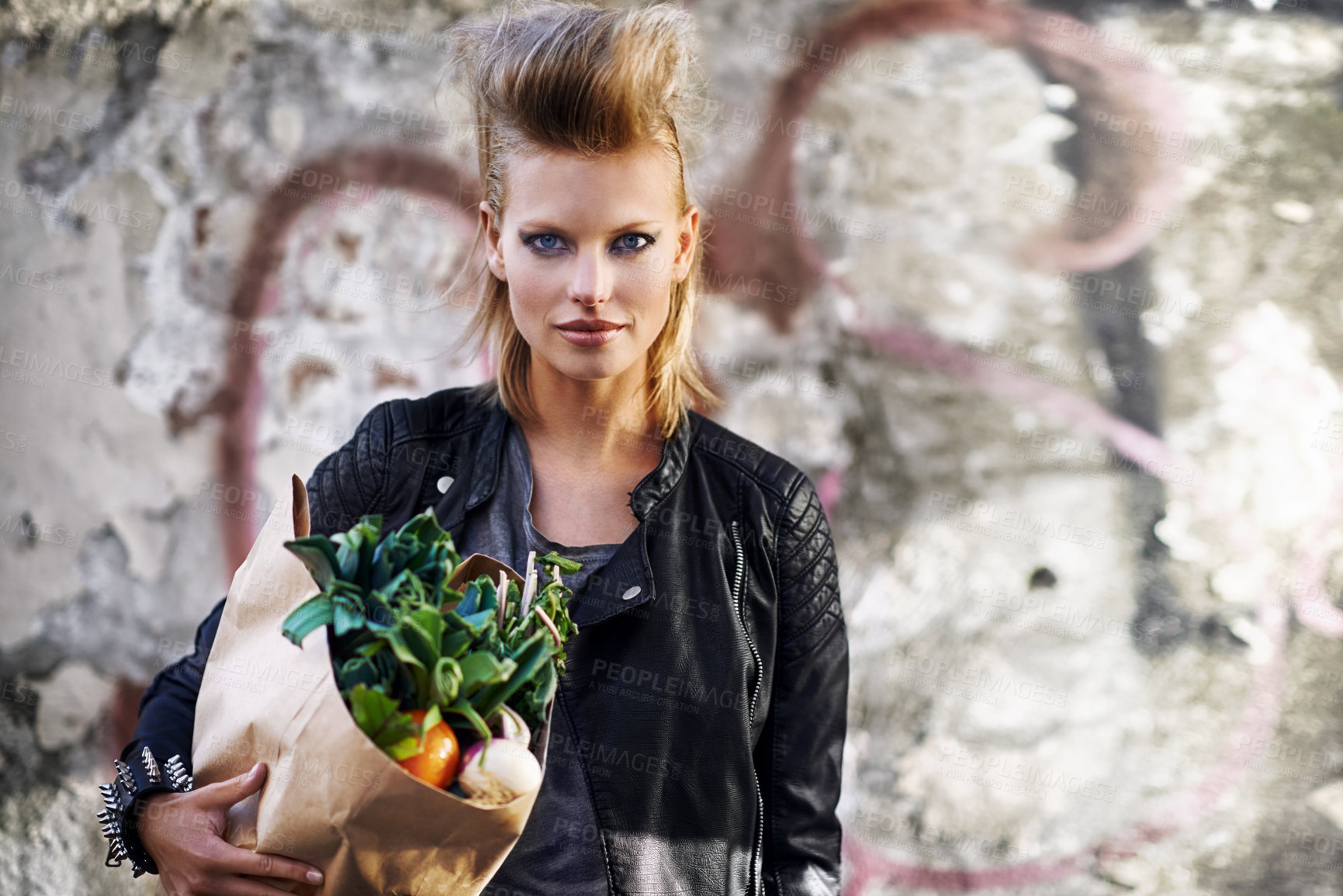 Buy stock photo Woman, portrait and fashion with vegetable grocery in city, cool and punk rock hairstyle in leather jacket by graffiti wall. California person, face and funky in town with food shopping by street art