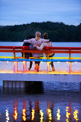 Buy stock photo Lake, bench and back of girl friends watching water in nature on vacation, adventure or holiday. Bonding, care and female friends embracing on wood chair in evening on outdoor weekend trip together.