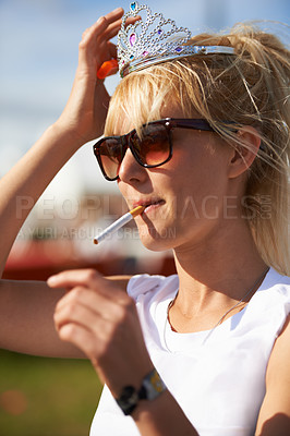 Buy stock photo Crown, smoking and young woman with cigarette in nature at outdoor festival, event or party. Fun, tiara and female person with tobacco, sunglasses and casual fashion in outside park or field.