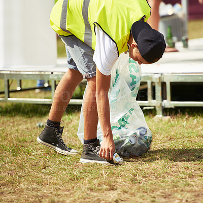 Buy stock photo Shot of a young man picking up garbage at an outdoor festival