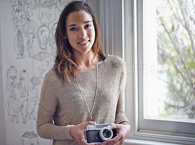 Buy stock photo A young photographer standing near a window while holding her camera