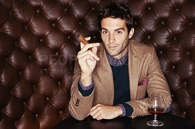 Buy stock photo Portrait of a handsome young man drinking and smoking a cigar in a club
