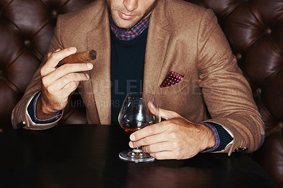 Buy stock photo A stylish man drinking whiskey and smoking a cigar