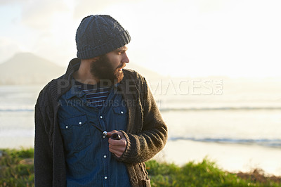 Buy stock photo Man, pipe and thinking in nature by ocean for ideas, vision or planning on winter morning. Male person, sunrise and standing on grass by sea for relaxation, wondering or smoking with tobacco outdoors