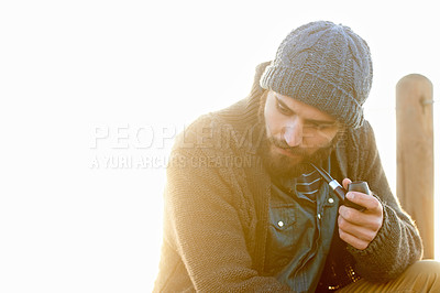 Buy stock photo Young, man and smoking a pipe in outdoor, thinking and tobacco habit in morning by sunrise. English guy, nicotine addiction and retro smoker for calm, satisfaction and vacation by ocean in cape town