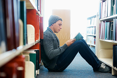 Buy stock photo A young man sitting on the floor and reading in a library