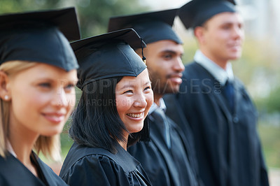 Buy stock photo Young college graduates holding their diplomas while standing in a row and smiling