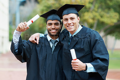 Buy stock photo Two young college graduates holding their diplomas while wearing cap and gown