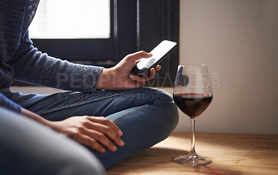 Buy stock photo Cropped shot of a woman sending a text message with a glass of wine beside her