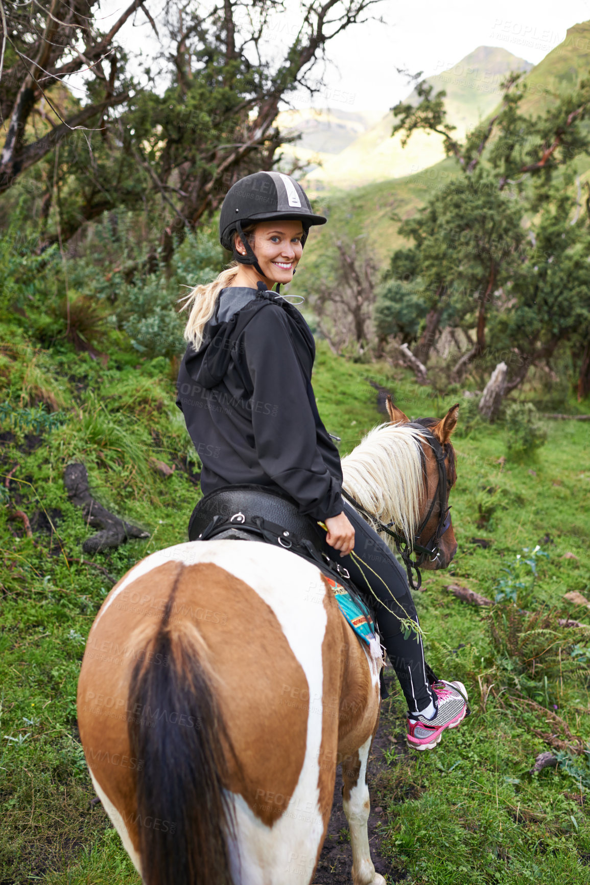 Buy stock photo An attractive young woman riding a horse on a mountain trail