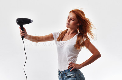 Buy stock photo Shot of a beautiful young woman blow drying her hair against a white background