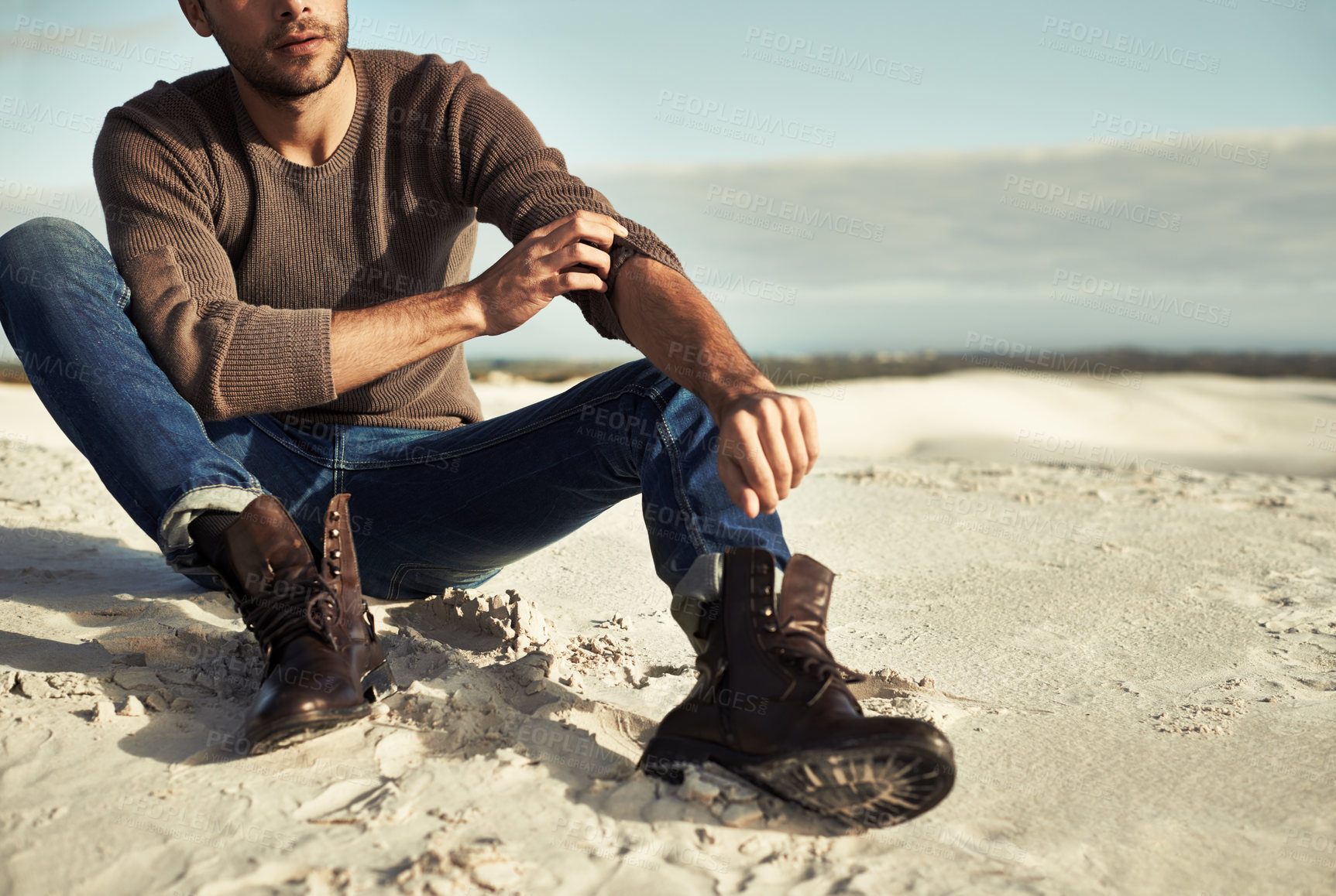 Buy stock photo A man wearing jeans and boots sitting on the beach
