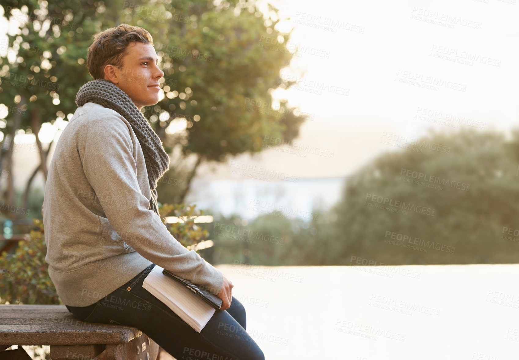 Buy stock photo Shot of a thoughtful young male student leaning on a campus bench