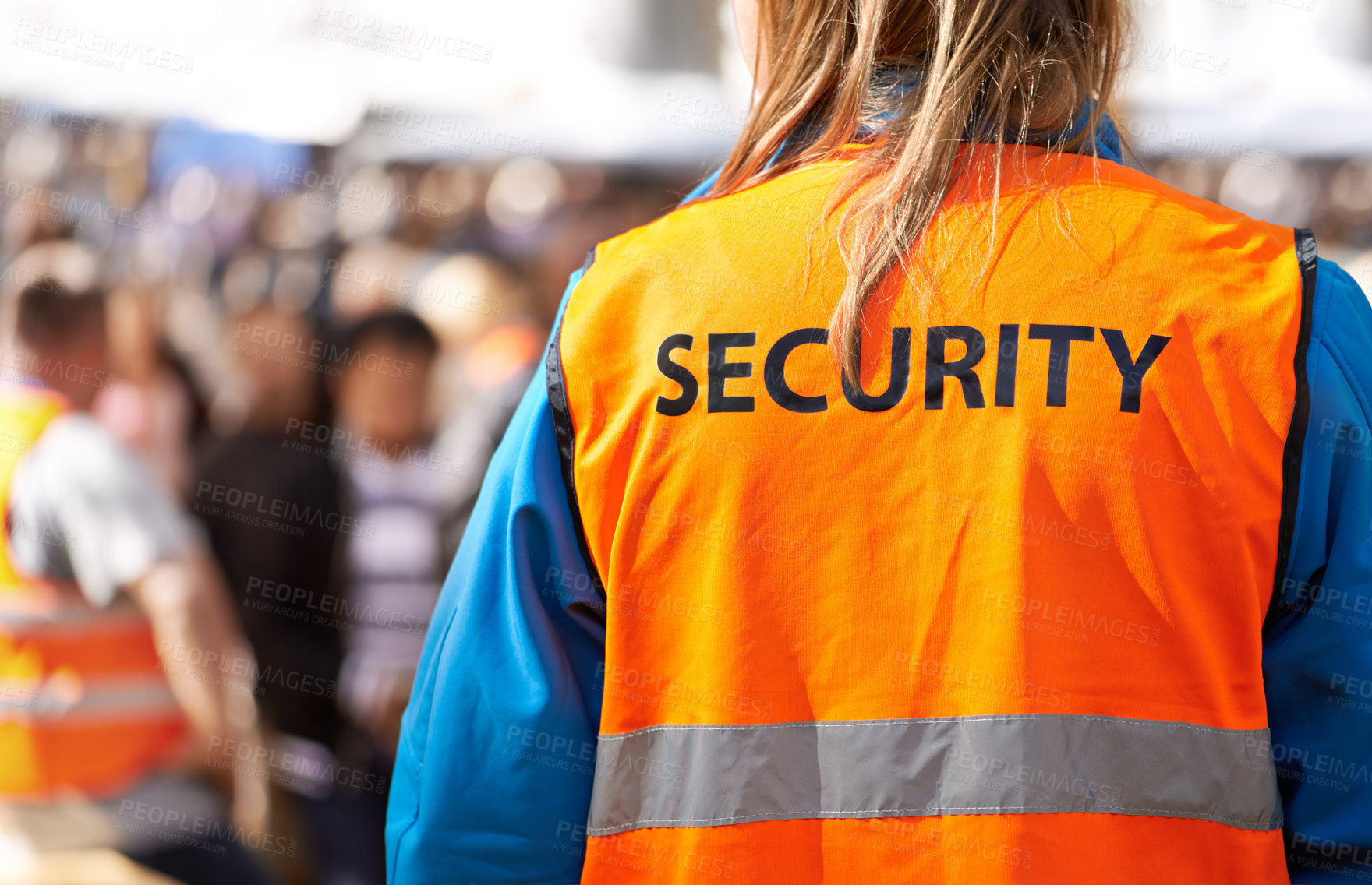 Buy stock photo Rearview shot of a security officer standing outdoors with a crowd in the background