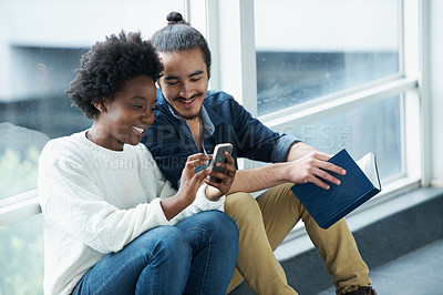 Buy stock photo A college couple sitting closely together looking at a message on one of their phones