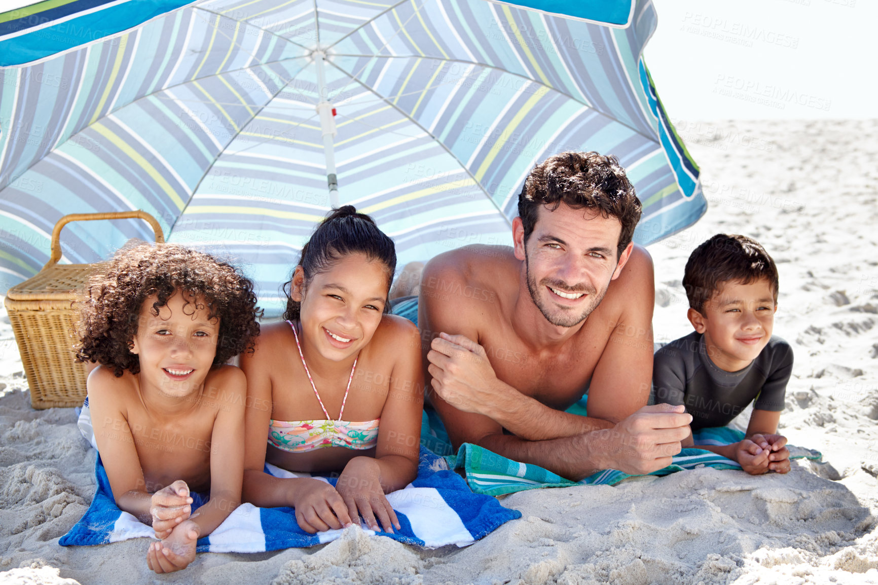 Buy stock photo Happy family, portrait and beach umbrella for bonding, vacation or outdoor holiday weekend together. Father, mother and children smile lying on sand for love, support or summer break by ocean or sea