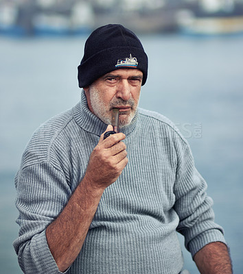 Buy stock photo Fisherman portrait, serious man and smoking pipe by the sea water at a port for fishing. Old man, ocean and senior dock worker sitting by boats outdoor with tobacco smoke at a harbor for work