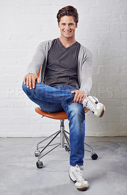 Buy stock photo Man, portrait and smile on chair with style on wall background for fashion, confidence or relax. Male person, face and sitting or casual in jeans in studio for happiness in Canada, clothes or outfit