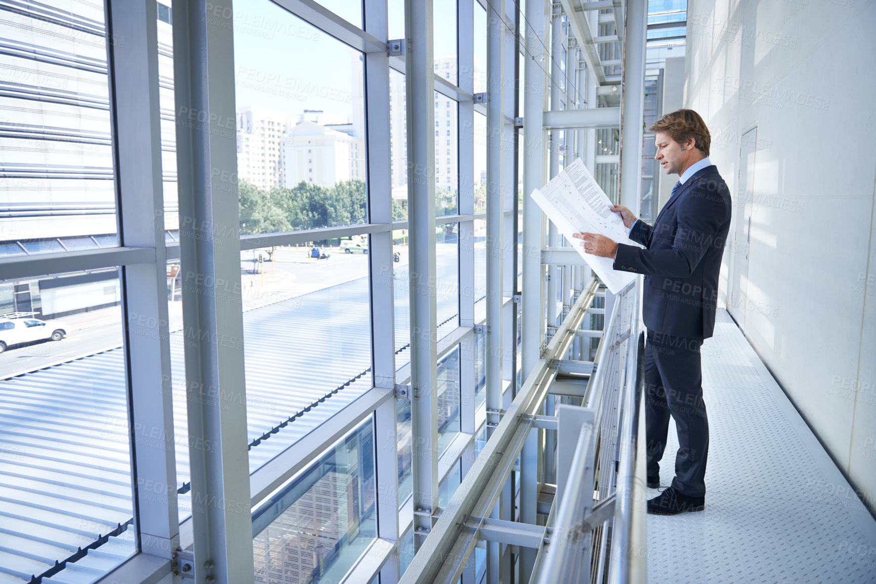 Buy stock photo Shot of a mature businessman looking at blueprints while standing near a window