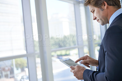 Buy stock photo Shot of a mature businessman standing in an office corridor using a digital tablet