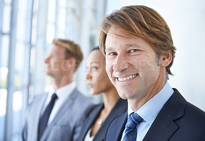 Buy stock photo A smiling businessman with two coworkers behind him
