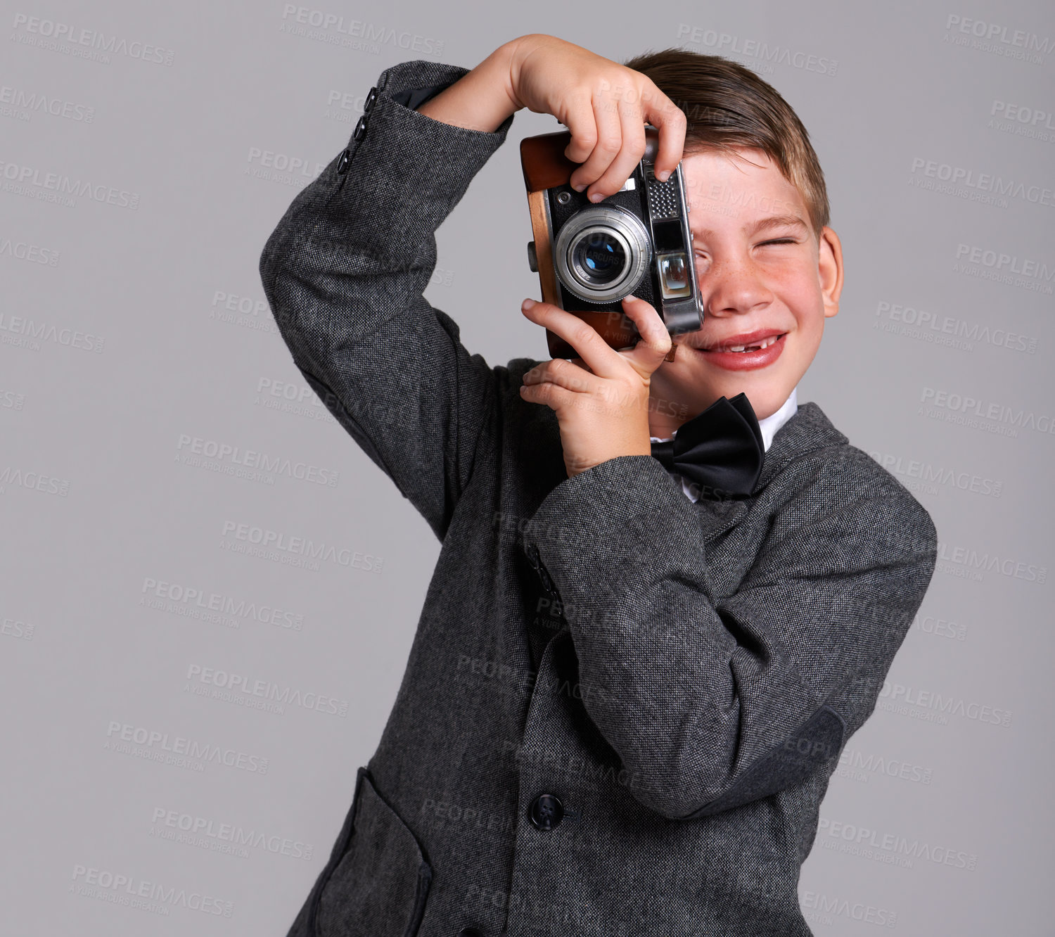 Buy stock photo Camera, photography and boy child in studio in elegant, classy or fancy suit outfit with smile. Happy, vintage and young kid with dslr equipment for picture with bowtie for fashion by gray background