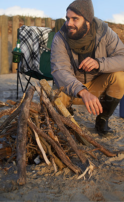 Buy stock photo Campfire, wood and man by beach on vacation, adventure or holiday camping for travel. Nature, outdoor and young male person sitting on chair in sand with flame for heat on weekend trip in winter.