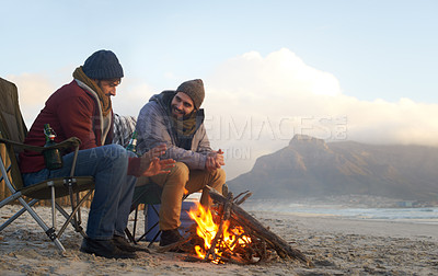 Buy stock photo Two young men sitting around a fire on the beach