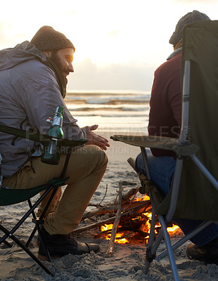 Buy stock photo Beach, beer and fire with man friends talking on coast or shore from back for travel, holiday or vacation. Nature, camping and sunset with happy young people together on sand by sea or ocean