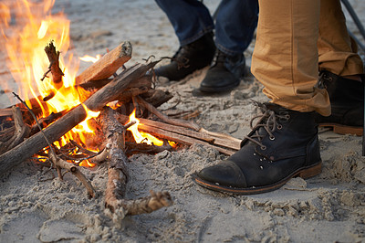 Buy stock photo Closeup, campfire and friends at the beach on holiday, vacation and travel to warm up in winter outdoor. Flame, wood and people together by sand at seashore with shoes, adventure and legs in nature