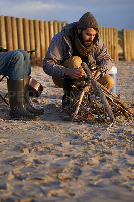 Buy stock photo A young man building a fire on the beach